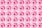 Arranged pink ring donuts whith glaze and white crumbs on a pink pastel background. Pattern. Flat lay