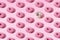 Arranged pink and white ring donuts with glaze and colorful crumbs on a pink pastel background. Pattern