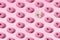 Arranged small pink and white ring donuts with pink and white glaze and colorful crumbs on a pink pastel background. Minimal