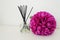Arrangement with incense sticks, essential oil in a glass vase and a bright pink-lilac terry artificial flower in the