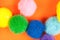 Arrangement of vivid colorful fluffy fuzzy textile soft balls on vibrant orange paper background