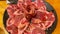 Array of raw meat pieces rests atop a plate on a wooden table