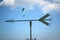 Arrow shape weathervane against summer`s sky with cumulus and paragliders in background, italian Alps. Italy