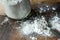 Arrowroot powder in a glass jar, spilled on a rustic wood table. Shown with tablespoon.