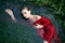 Art beautiful romantic portrait of a sexy young woman in a red dress lying in a river with green algae in summer in
