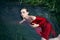 Art beautiful romantic portrait of a sexy young woman in a red dress lying in a river with green algae in summer in