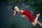 Art beautiful romantic portrait of a sexy young woman in a red dress lying in a river with green algae in summer in
