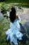 Art beautiful romantic woman lies in swamp in blue long dress with flowers. Portrait brunette in transparent dress in water swamp