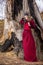 Art Photography Concepts. Mysterious Beautiful Fairy Medieval Princess in Red Dress and Spiky Black Crown in Forest in Early