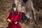 Art Photography. Mysterious Fairy Medieval Queen in Red Dress and Spiky Black Crown Posing With Ancient Book in Forest in Early