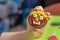 Art work done by a child. A cinnamon round cookie decorated by a child. A smiling face painted with colorful iced felt-tip pens.