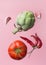 Artichoke ripe juicy tomato hot chili peppers garlic cloves floating levitating on pink background. Creative food poster