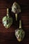 Artichokes: Top view of three fresh artichokes on a dark wood surface. Light Painting Still Life