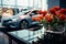 Artificial blooms adorn a glass table in a sleek car showroom.