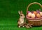 An artificial Easter gray rabbit is standing near a wicker basket with chicken eggs and a willow on the right. copyspace