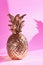 Artificial gold colored pineapple on pink background