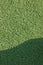 Artificial grass fake turf synthetic lawn field macro closeup with gentle shaded shadow area, green sports texture background