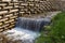 Artificial waterfall on mountain stream against protect wooden logs wall