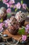 Artisan chocolate eggs adorned with colorful sprinkles, wooden surface amidst delicate pink flowers, Easter confections