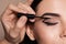 Artist applying black eyeliner onto woman`s face on beige background, closeup