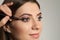 Artist applying black eyeliner onto woman`s face on grey background, closeup