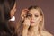 An artist applying eyeshadow powder with a brush for smokey eyes makeup on a pretty woman. Face close-up. Makeup lessons