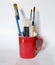 Artist brush, pencil, watercolor brush in a red cup on a white background