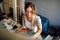 Artist female sitting next to the easel with canvas painting something in her art studio. A professional candid young woman