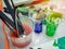 Artist paint brushes in white bucket of water, acrylic colour in plastic cups