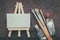 Artist paintbrushes, paint tubes and small easel with canvas closeup. Top view.