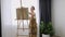 Artist paints on canvas and smears a brush. Canvas stands on the easel. Woman drawing at easel. Female painting at studio