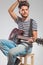 Artist playing guitar seated on chair while fixing his hair