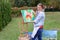 Artist woman holds painting and looks at it, posing at camera an