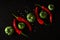 artistic combination of alternating chili peppers and green tomatoes with coarse sea salt on a black plastered surface arranged