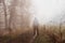 An artistic, double exposure of a hooded man standing on a spooky rural path on a foggy winters day. With a grunge, blurred edit