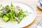 Arugula salad with bean sprout, enoki mushrooms, cucumber and purple edible flowers, over an oak wood background.