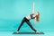 Asanas coach young and active blonde woman practicing yoga and meditating on a yoga mat in studio on blue background