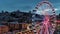 ascending aerial footage of SkyStar Ferris Wheel with lights at sunset, people walking and cars driving on the street