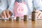 Ascending coin towers stand on table against background of pink piggy bank.