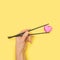 Asia artisan food concept. The man\\\'s hand holding chopsticks with pink heart shaped french yummy macaron. Yellow backgroun