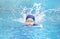 Asia cute boy wearing swimming suit and goggles used foam to practice swimming in swimming pool. Healthy kid enjoying active