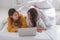 Asia lesbian lgbt couple lying on bed using laptop computer together near white window sunlight in bedroom with happiness moment