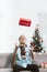 Asia man wear santa hat sit on sofa throw red gift box in air wi