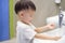 Asian 2 - 3 years old toddler baby boy child washing hands by himself on sink and water drop from faucet in public toilet