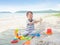 Asian 2 years old toddler boy sitting & playing children`s beach toys on sandy tropical beach