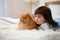 Asian 3-years child lying on white bed together with brown Pomeranian