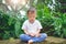Asian 30 months / 2 years old toddler baby boy child with eyes closed, barefoot practices yoga & meditating outdoors on nature