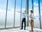 Asian architect Male and female inspecting construction work inside high-rise building near huge window glass on sky background