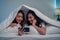 Asian attractive lesbian couple use mobile phone watch movie on bed. Beautiful sibling in pajamas lying down with blanket in