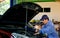 Asian automotive mechanic with blue uniform use wrench to fix the problem in part of engine around bonnet and front bumper of car